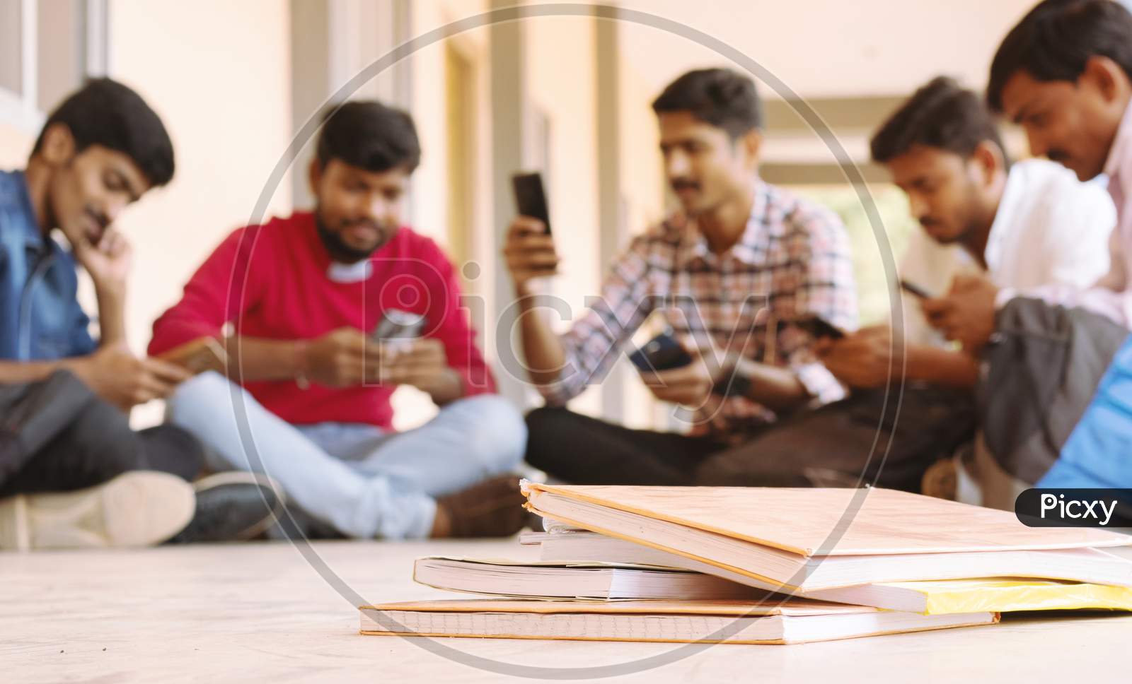 Selective Focus Of Books, Group Of Students Busy On Mobile By Avoiding Books During Exams At College - Teenager Students On Smartphone Video Game Addiction Concept.