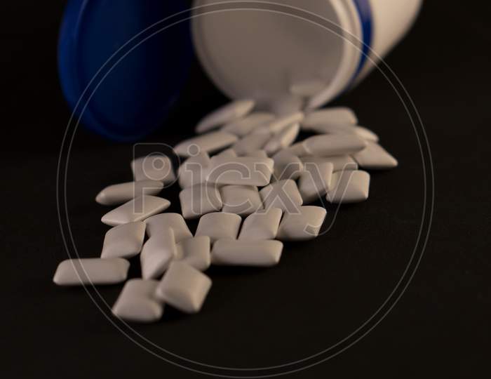 Gum in a bottle on a black background. Scattered chewing gum in the form of pads.