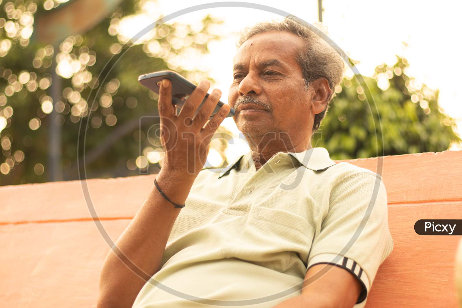 An old man or Elderly man talking to a mobile-phone at the outdoors