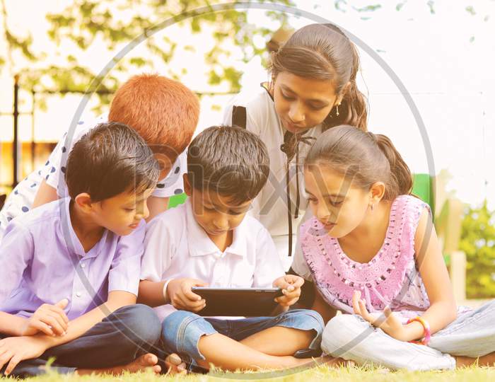 Children Busy In Using Mobile Phone At Park - Concept Of Kids On Mobile Devices And Technology Addiction - Young Teens Using Technology, Internet On Smartphone.