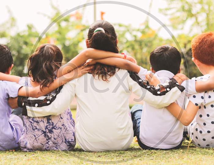 Back View, Group Of Kindergarten Multi Ethnic Kids Friends Arm Around Sitting Together At Park Outdoor - Concept Showing Of Childhood Friendship, Togetherness With Diversities.