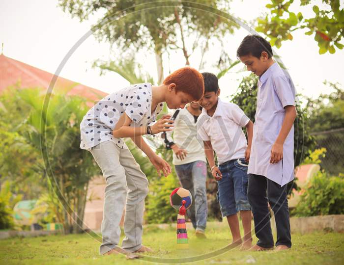 Children Playing Lagori, Dikori Or Lagoori Outdoor Traditional Game, Where Two Teams Try To Hit A Pile Of Stones With Ball - Concept Of Kids Enjoying Outdoor Games In Technology Driven World.