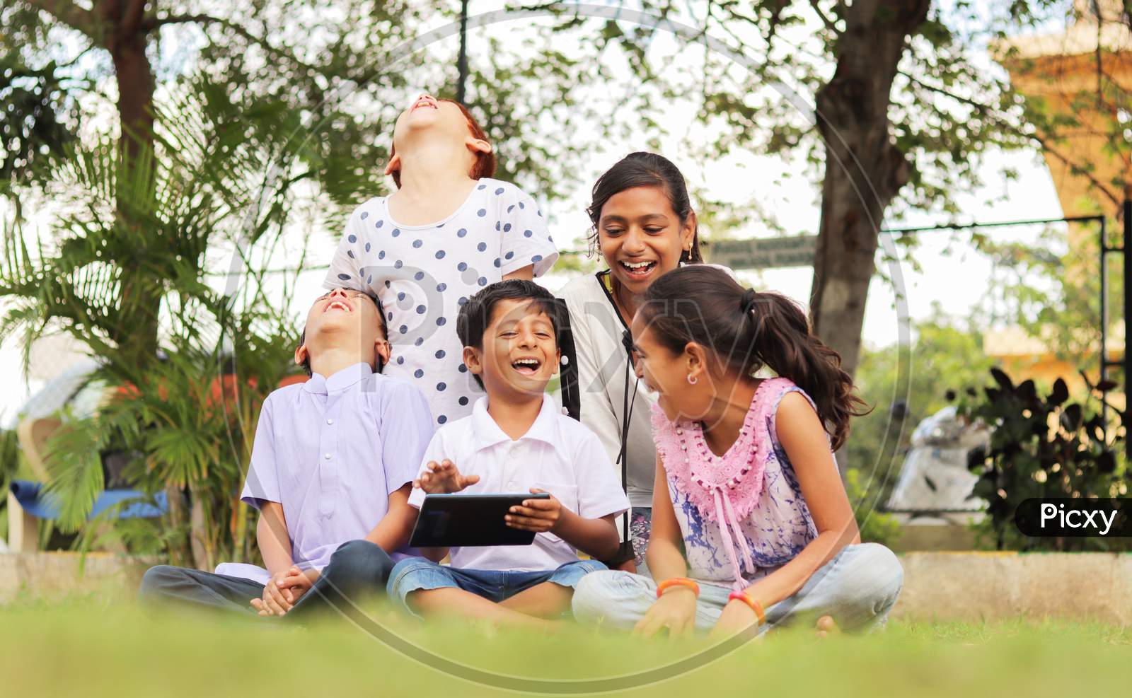 Group of Children using a Mobile or Smartphone and Laughing loudly in a Park or Outdoors