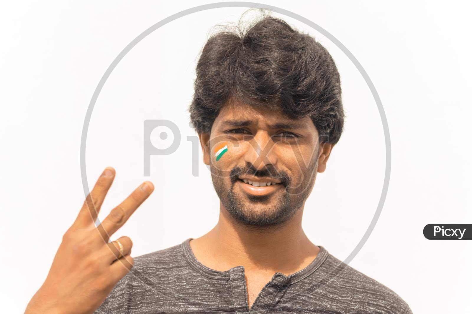 Portrait Of Young Cheerful Indian Male Cricket Sports Fan Painted Indian Flag On His Face And Showing Hand Gesture Of Victory