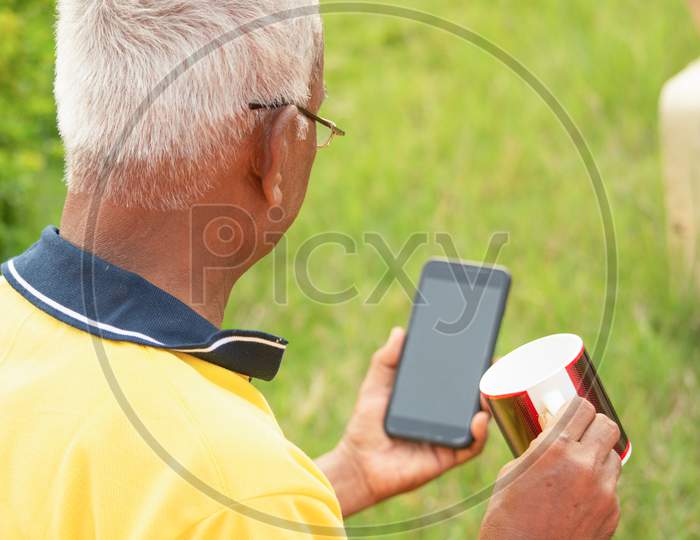 An old man or Elderly man using a mobile holding the cup in a park
