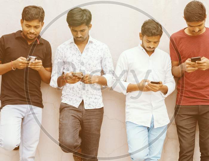 Young People With Heads Down Busy On Smart Phone - Friends Group Using Smartphone Againt Wall At Backyard - Concept Of Millennials Addicted And Connected Always To Technology.