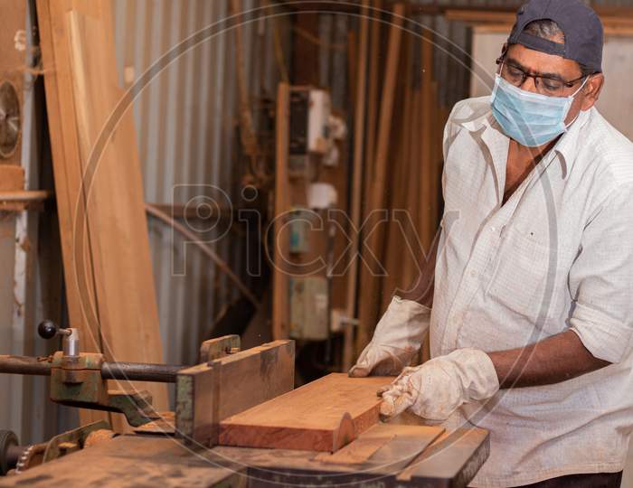 A Carpenter cutting Large Wooden Board with A Mask due to Pandemic or Corona Virus Effect