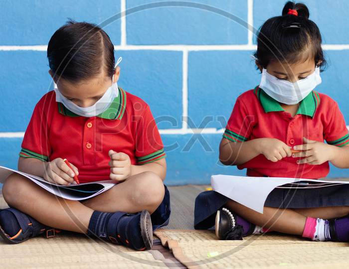 Kids Busy In Writing With Medical Face Mask Wearing Due To Covid-19 Or Coronavirus Outbreak Or Pandemic At School
