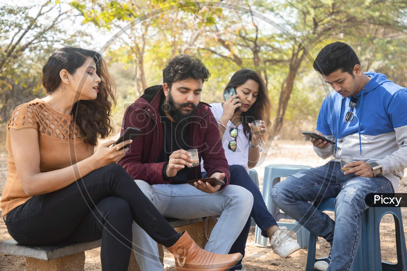A Group of Happy Young People using Mobile Phone or Smartphone At Outdoors
