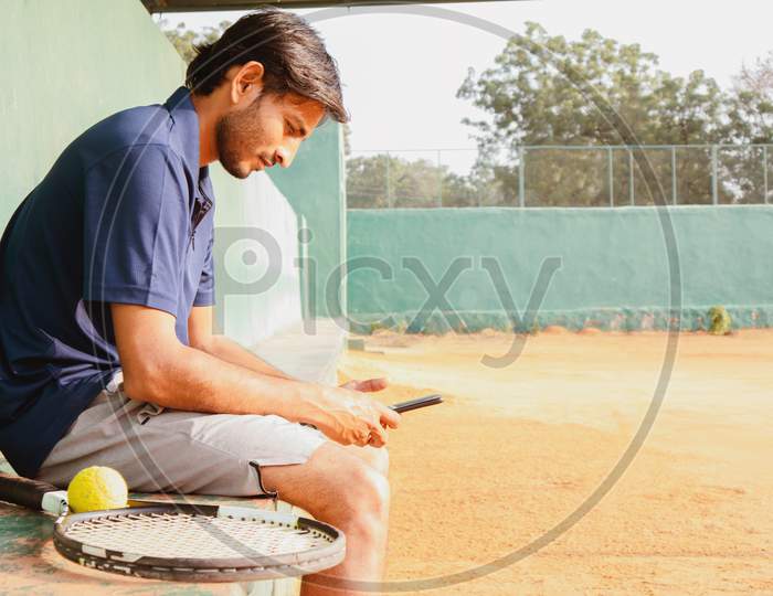 Young Indian Man using a Smartphone  in a Tennis Court