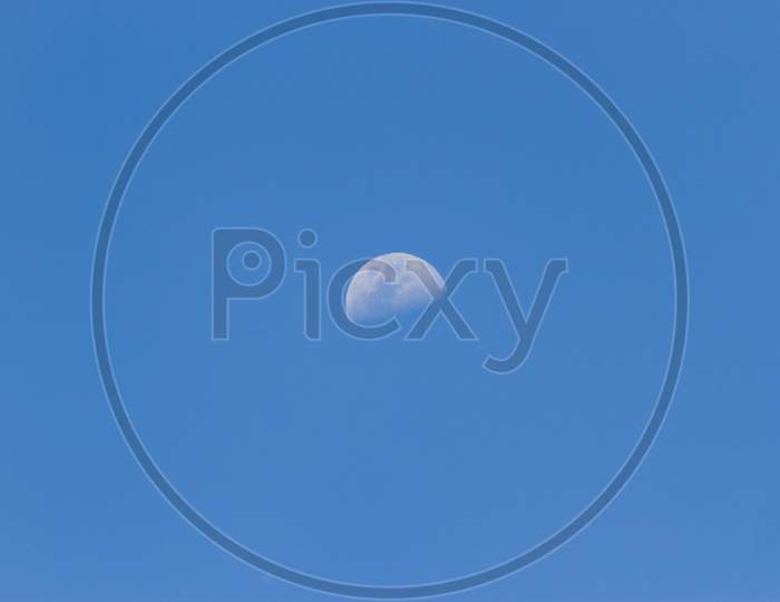 A Horizontal Shot Of A Half-Moon Visible During Daylight In The Blue Sky