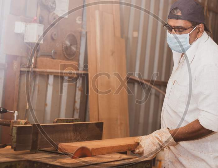 A Carpenter cutting a Large Wooden Piece with Mask during Corona Virus Pandemic