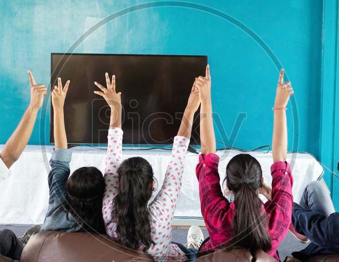 Back View of Happy Young People Cheering while watching Television