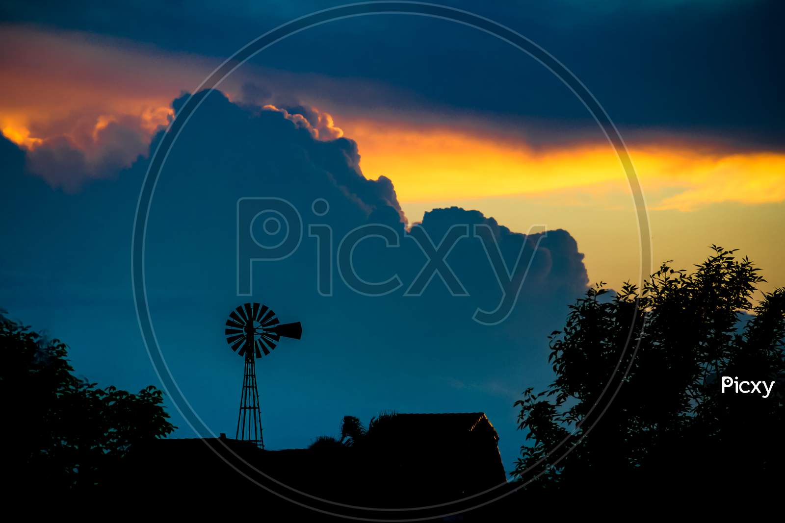Landscape With Sky Laden With Storm Clouds With Yellow And Blue Orange Colors And Windmill Silhouette