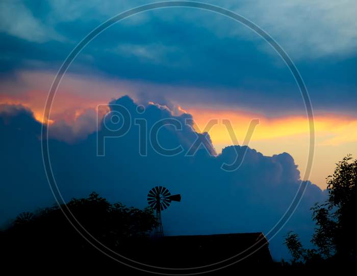 Landscape With Sky Laden With Storm Clouds With Yellow And Blue Orange Colors And Windmill Silhouette