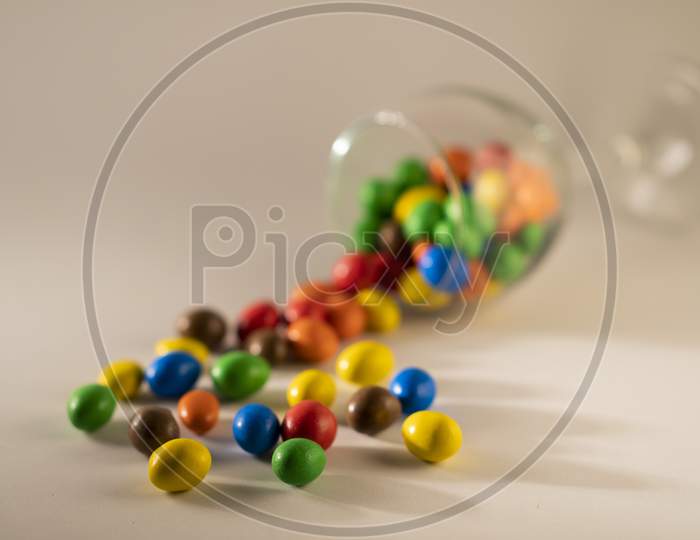 Scattered multicolored chocolate candy or candy balls with a depth of field view on a white blurred  background .