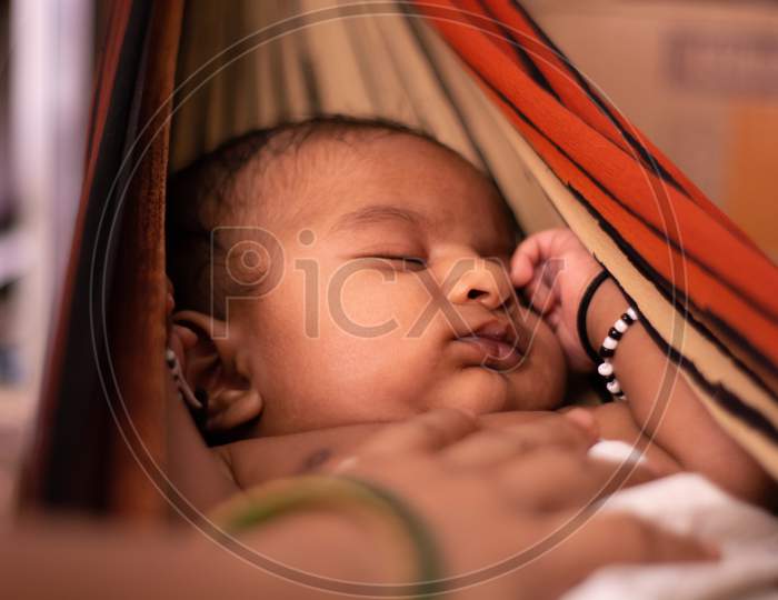 Closeup Of Cute Little New Born Baby Sleeping In Cradle Made Of Saree With Mothers Hand On Baby.