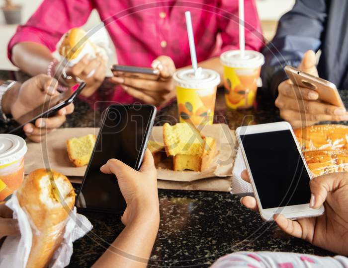 A Group of Young People using Mobile Phone or Smartphone While having their Food