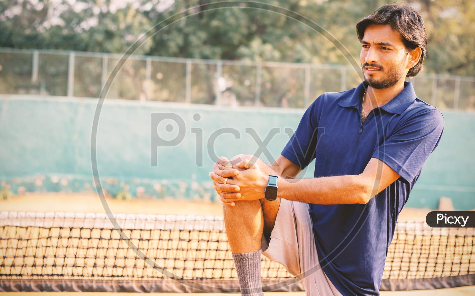 Young Tennis Player Stretches Legs Before Playing At Tennis Court - Concept Of Warming Up Before Playing Any Sports.