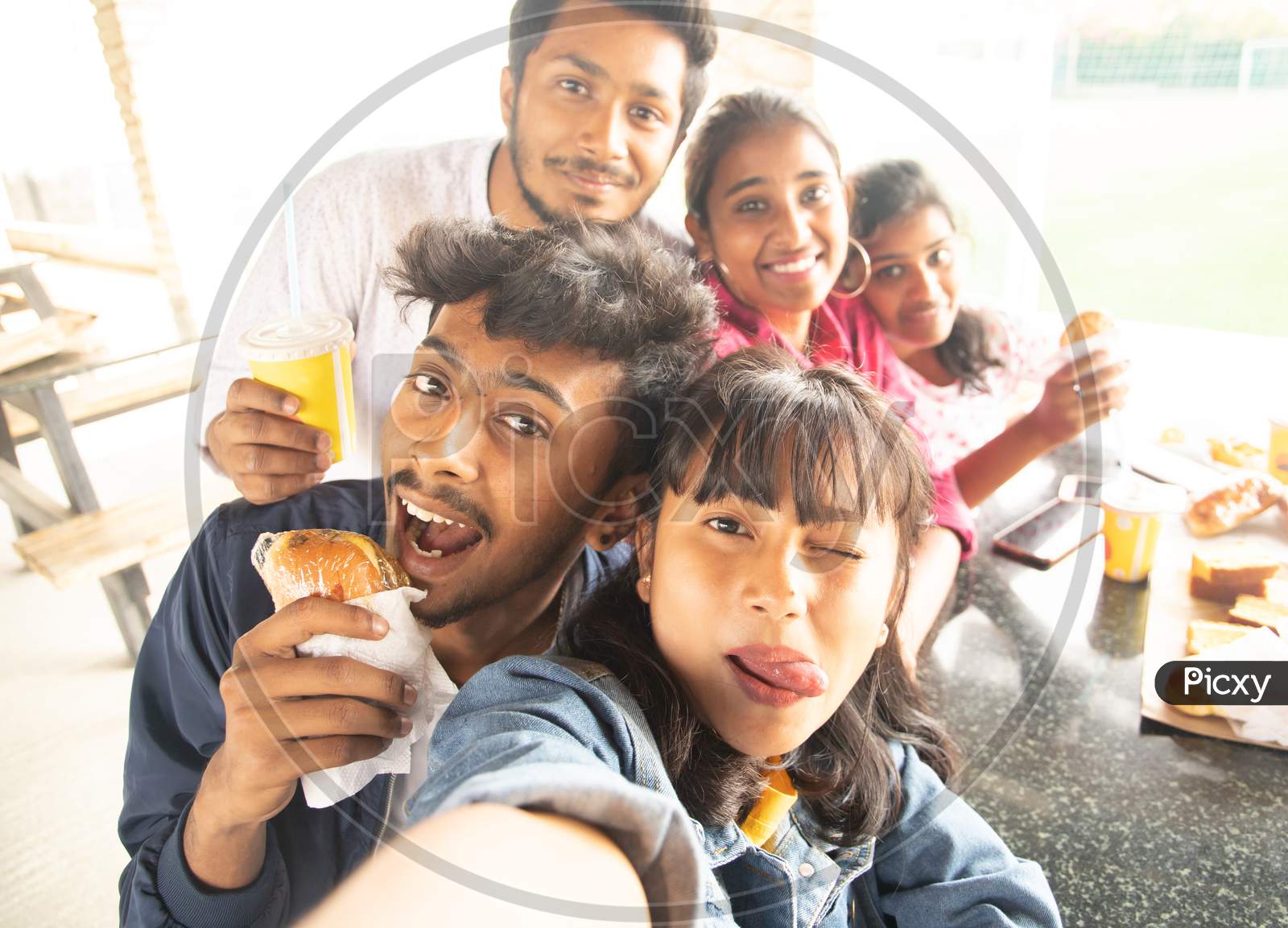 A Group of Young People Taking Selfies using Mobile phones or Smartphone While having their Food
