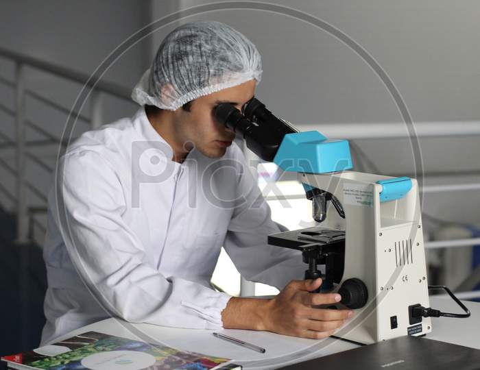 A SCIENTIST IS RESEARCHING WITH MICROSCOPE TO FIND A MEDICINE.