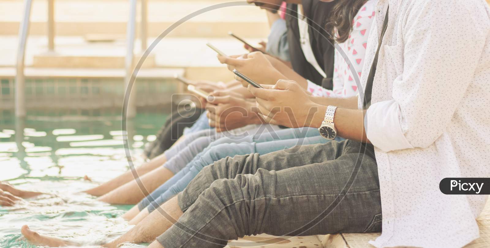 A Group of Young People using Mobile phones or Smartphone At Outdoors in a Pool