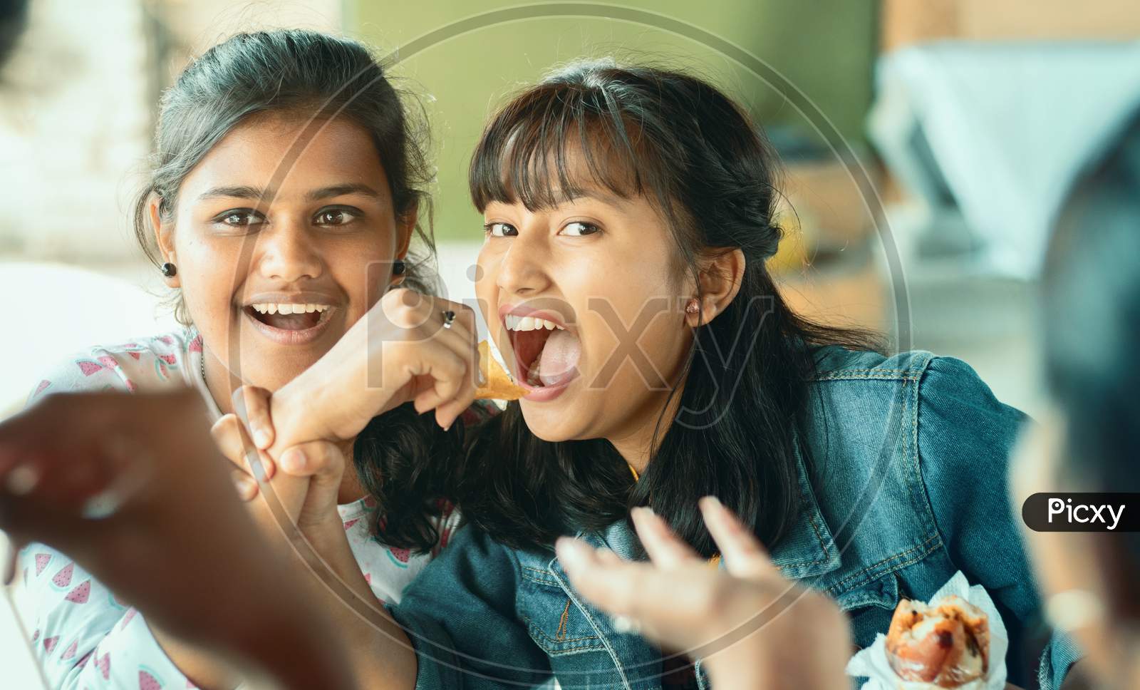 Teenager Trying To Take Or Grab Food From Friend - Young Girl Playfully Fighting For Snacks With Her Friend - Concept Of Friends Having Fun While Having Food At College Restaurant.