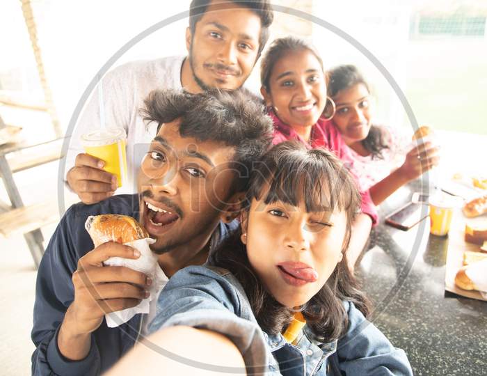 A Group of Young People Taking Selfies using Mobile phones or Smartphone While having their Food