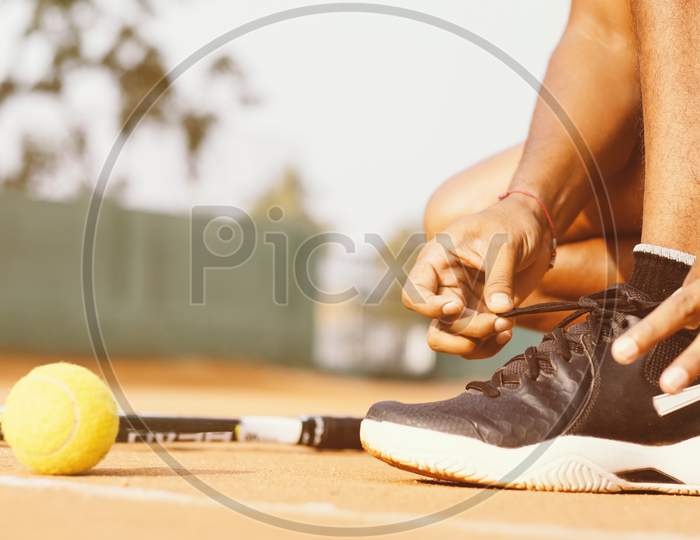Close up shot of a  Young Indian Man tying Shoelace in a Tennis Court
