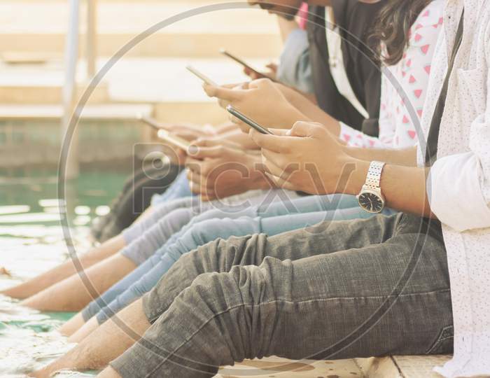 A Group of Young People using Mobile phones or Smartphone At Outdoors in a Pool