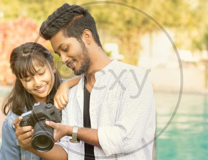 Cute Couple Looking Pictures On Camera Screen - Happy Young Professional Photographer Showing Images To Model On His Dslr - Concept Of Model And Cameraman Working Together.