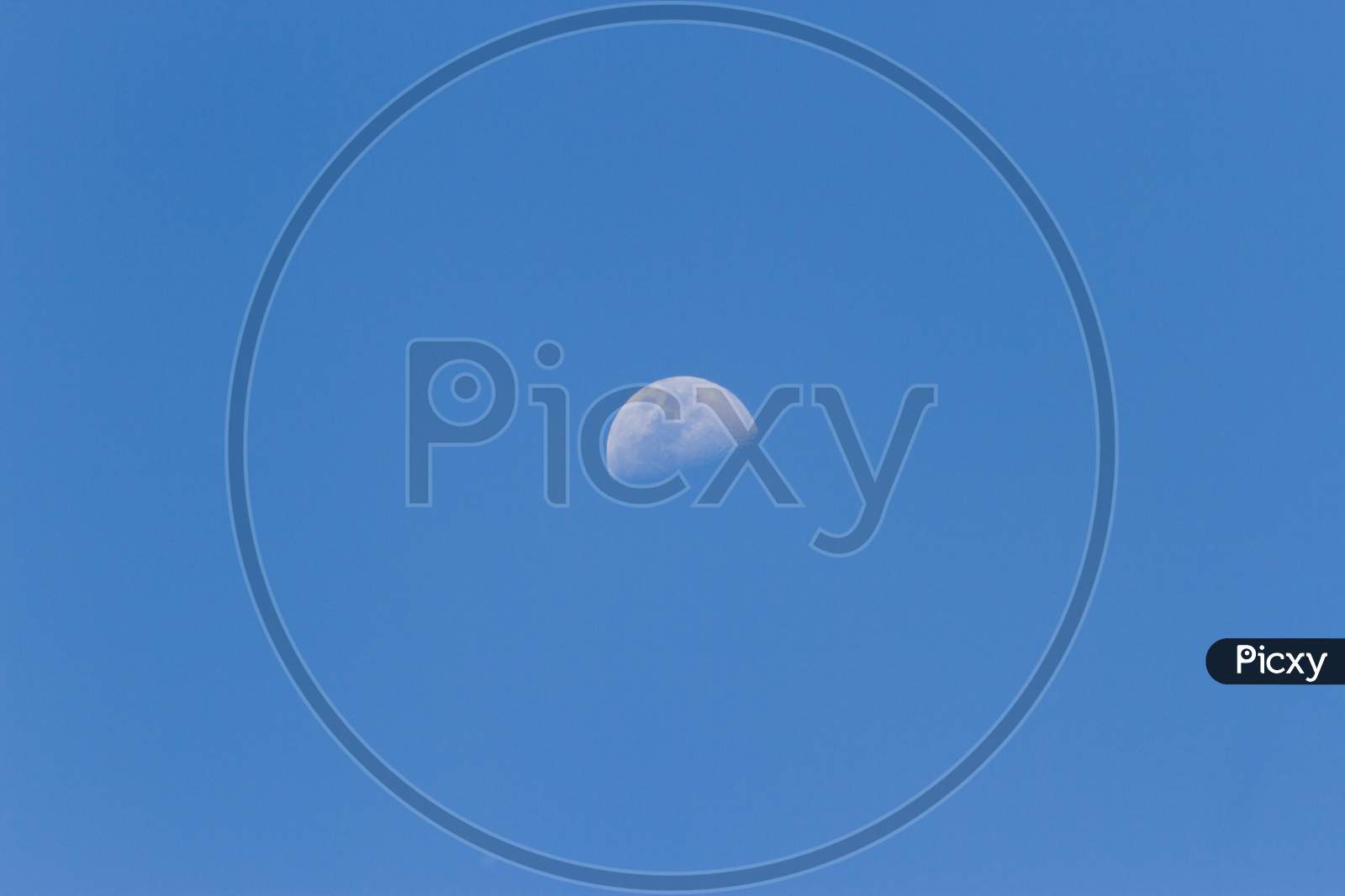 A Horizontal Shot Of A Half-Moon Visible During Daylight In The Blue Sky
