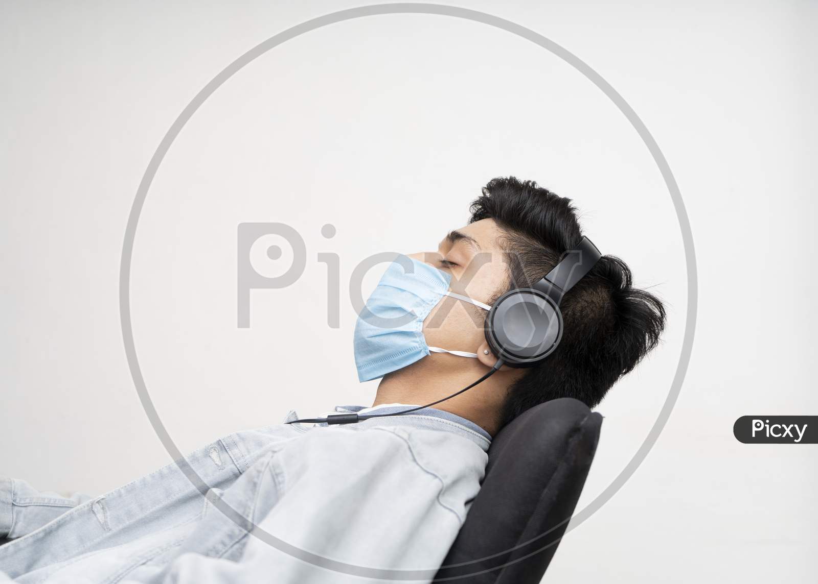 Vyoung Asian Boy Wearing A Blue Surgical Mask For Protection From Covid-19, Sleeping On A Chair While Listening To Music.