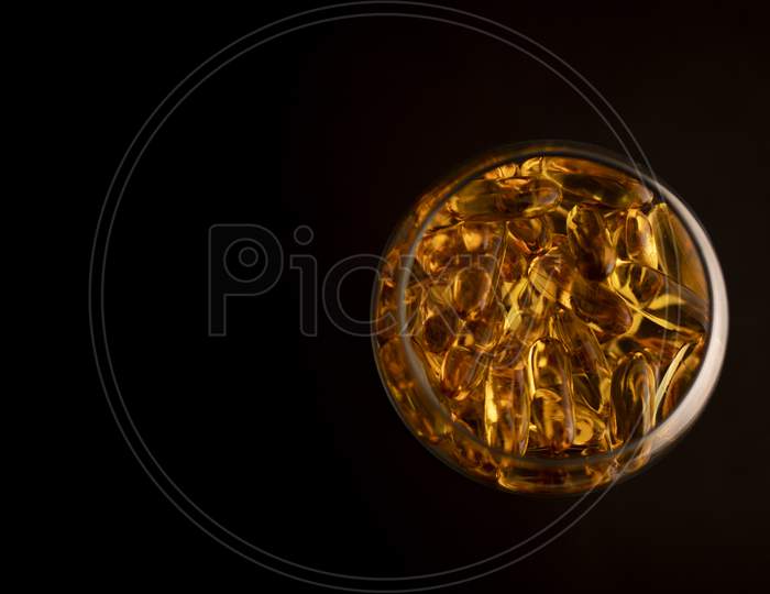 Omega-3 capsules in a glass on a black background.