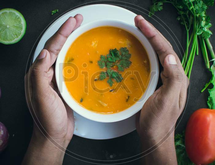 A Pair Of Hands Hold A White Soup Bowl Filled With Thai Soup Decorated With Coriander Leaves