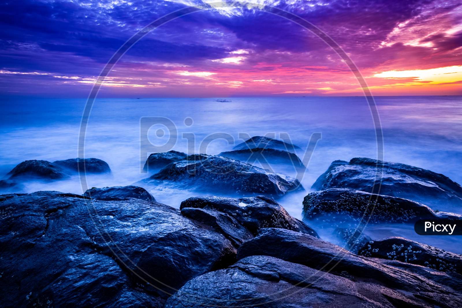Beautiful Sunrise Over The Beach In Long Exposure. Moving Elements Sunrise And Wave Photography From The Rocky Beach In India. Red Sky In Bay Of Bengal , Slow-Shutter Sea Waves And Rocks Photography.