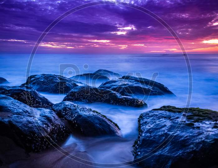 Beautiful Sunrise Over The Beach In Long Exposure. Moving Elements Sunrise And Wave Photography From The Rocky Beach In India. Red Sky In Bay Of Bengal , Slow-Shutter Sea Waves And Rocks Photography.