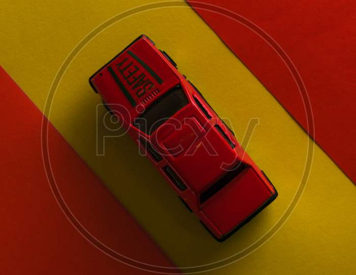 A red toy car is isolated in yellow background surrounded by red border.