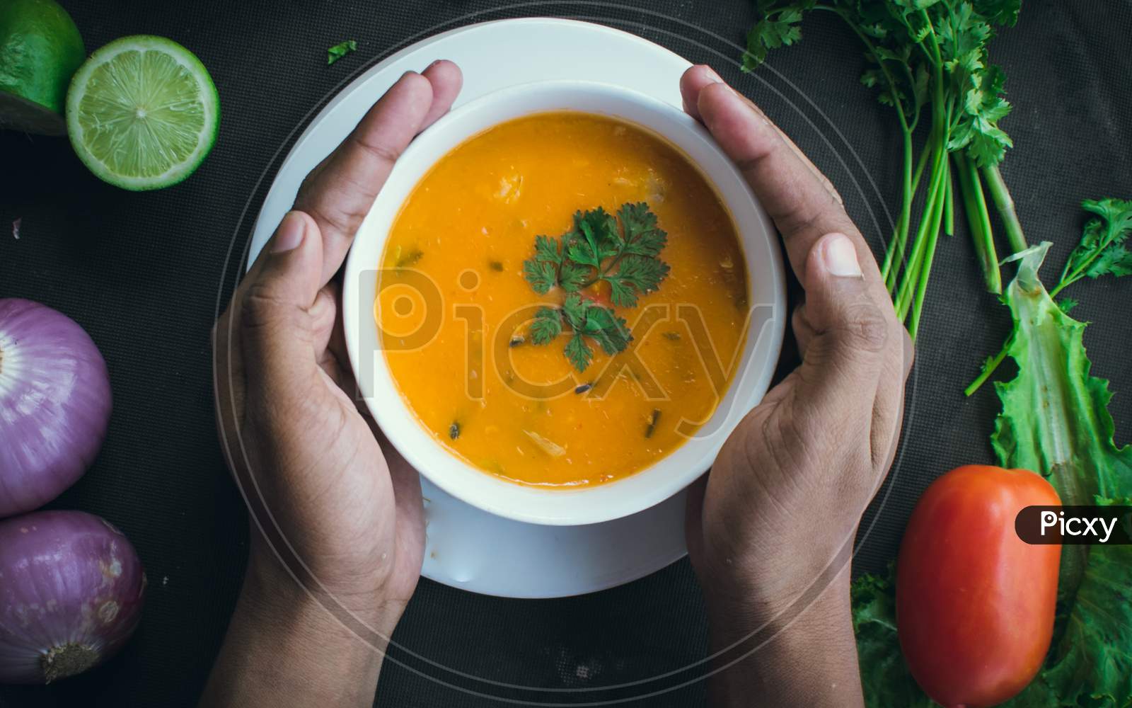 A Pair Of Hands Hold A White Soup Bowl Filled With Thai Soup Decorated With Coriander Leaves