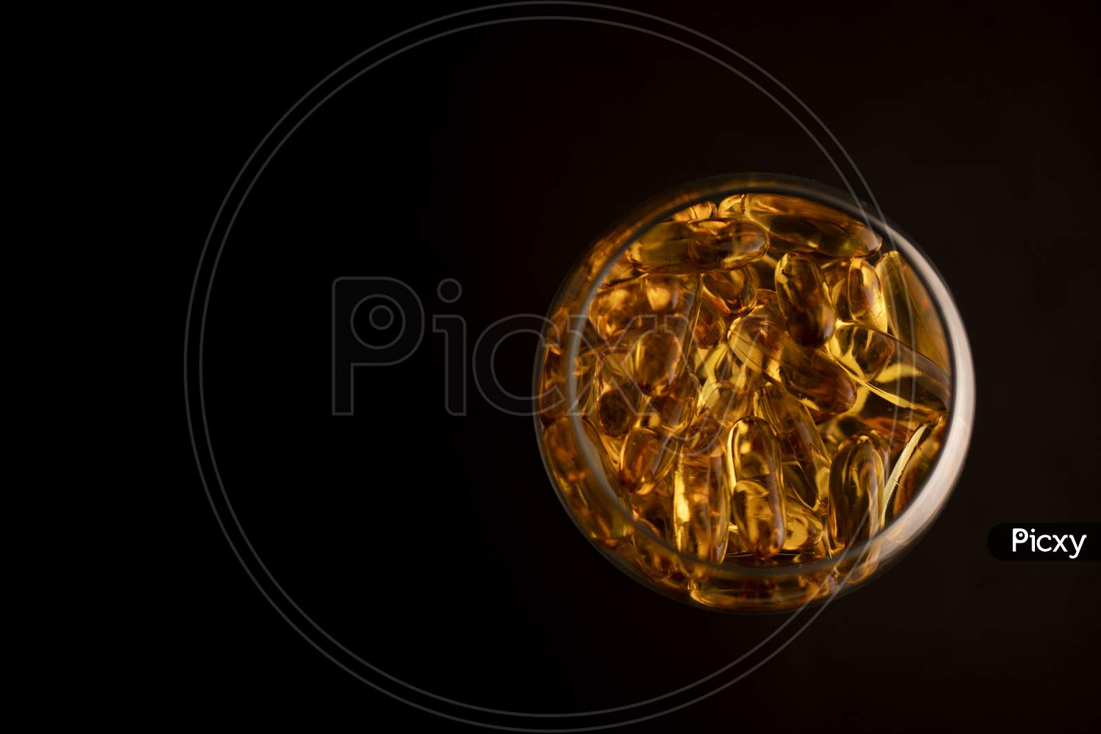 Omega-3 capsules in a glass on a black background.