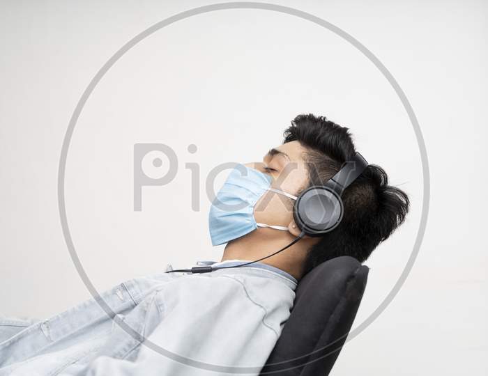 young Asian Boy Wearing A Blue Surgical Mask For Protection From Covid-19, Sleeping On A Chair While Listening To Music.