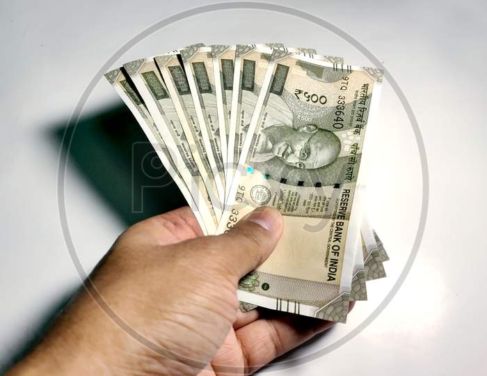 Hand Holding Five Hundred Indian Rupee Notes Against White Background