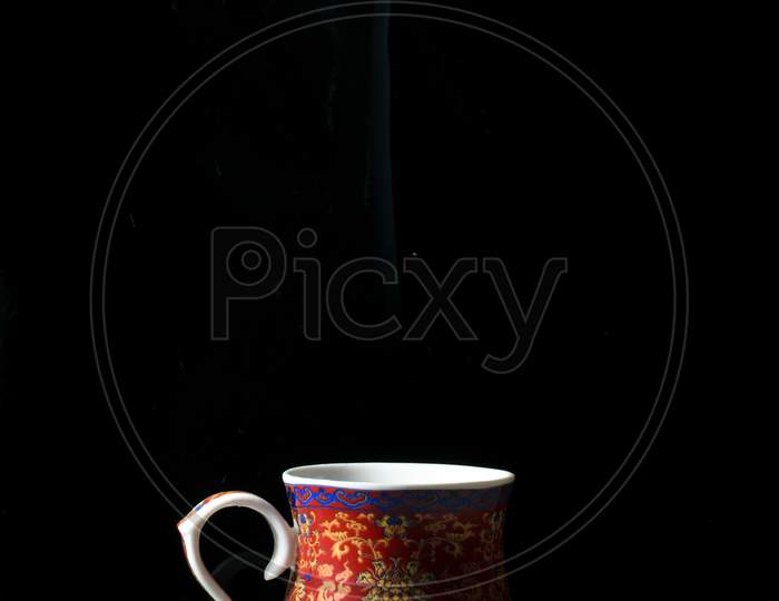 A Red Tea Cup With Designs On It Placed On A White Reflective Table And Smokes Of Hot Tea Coming Out Of It