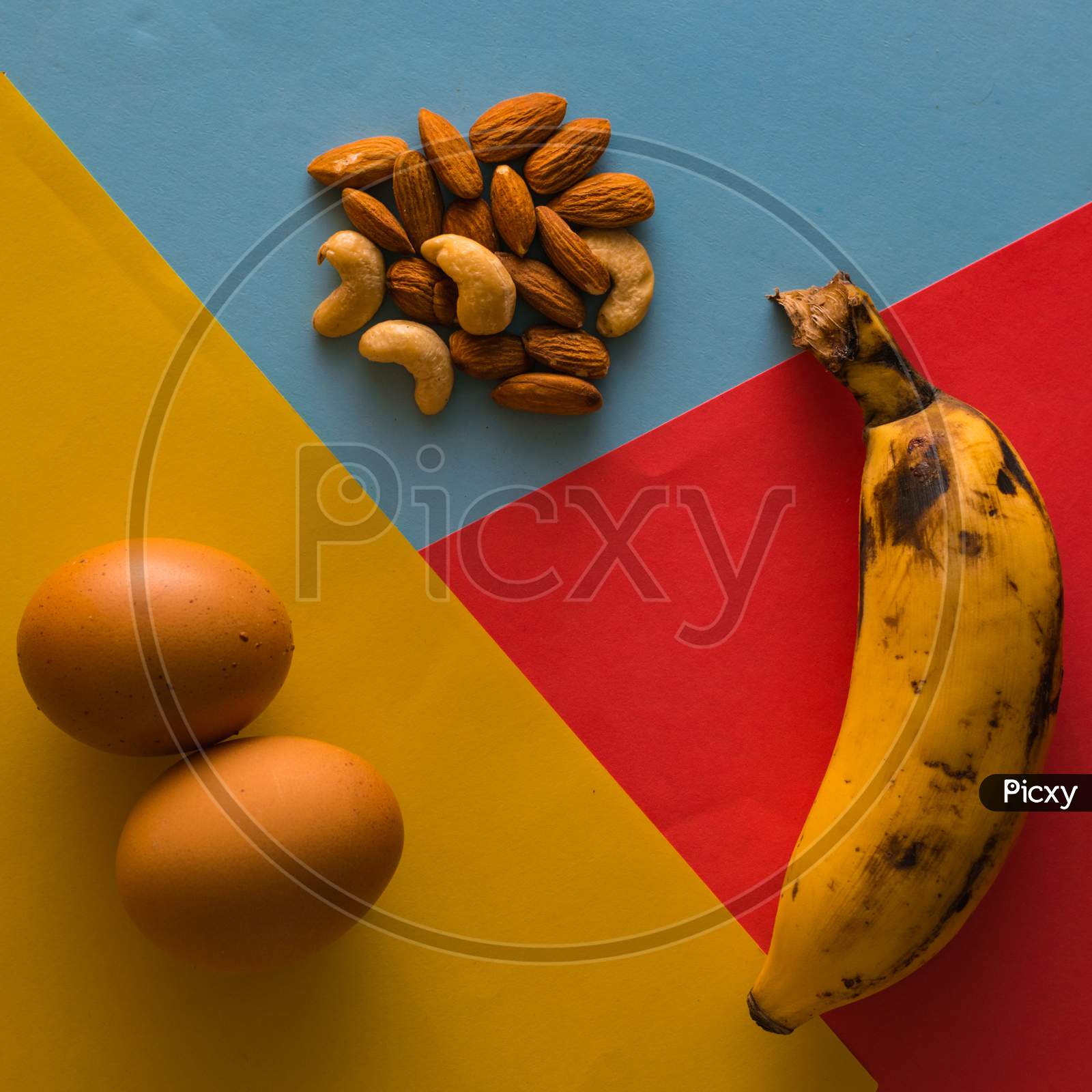 Balanced Diet Food Using Egg,Banana And Various Nuts On Plain Background