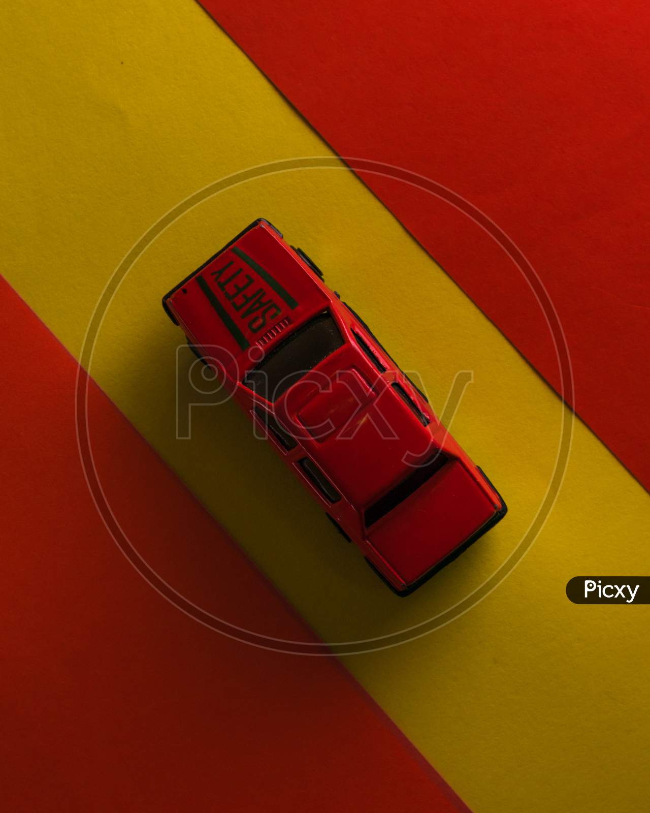A red toy car is isolated in yellow background surrounded by red border.