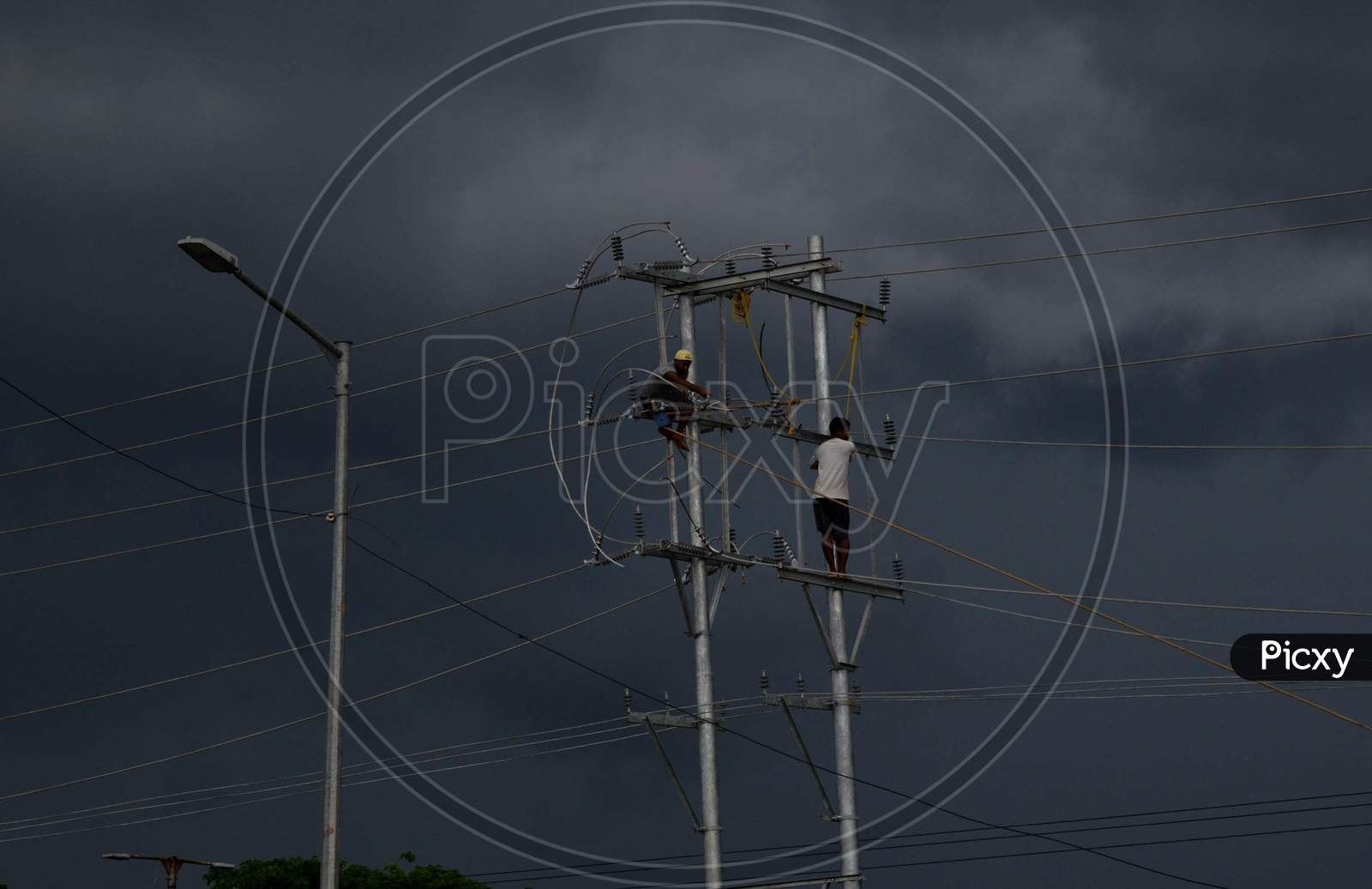 Labourers Work On An Electric Pole As Dark Clouds Cover Over The Sky, In Guwahati On Saturday, June 13, 2020.
