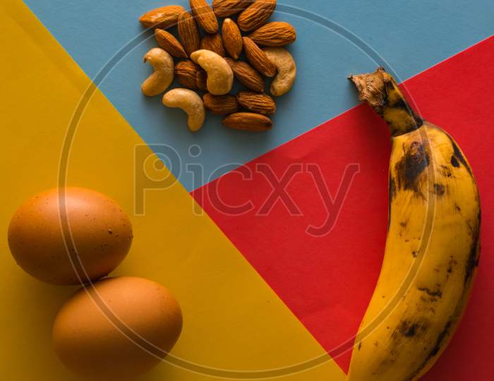 Balanced Diet Food Using Egg,Banana And Various Nuts On Plain Background