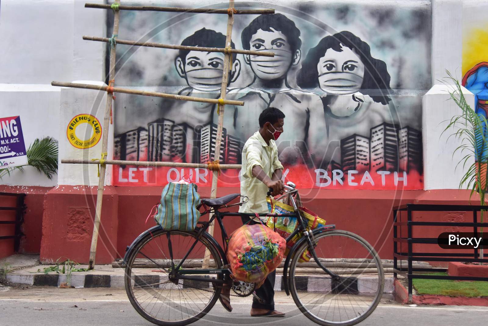 A Man Carries Goods On His Bicycle As He Walks past a Mural in Guwahati , India On June 14,2020.