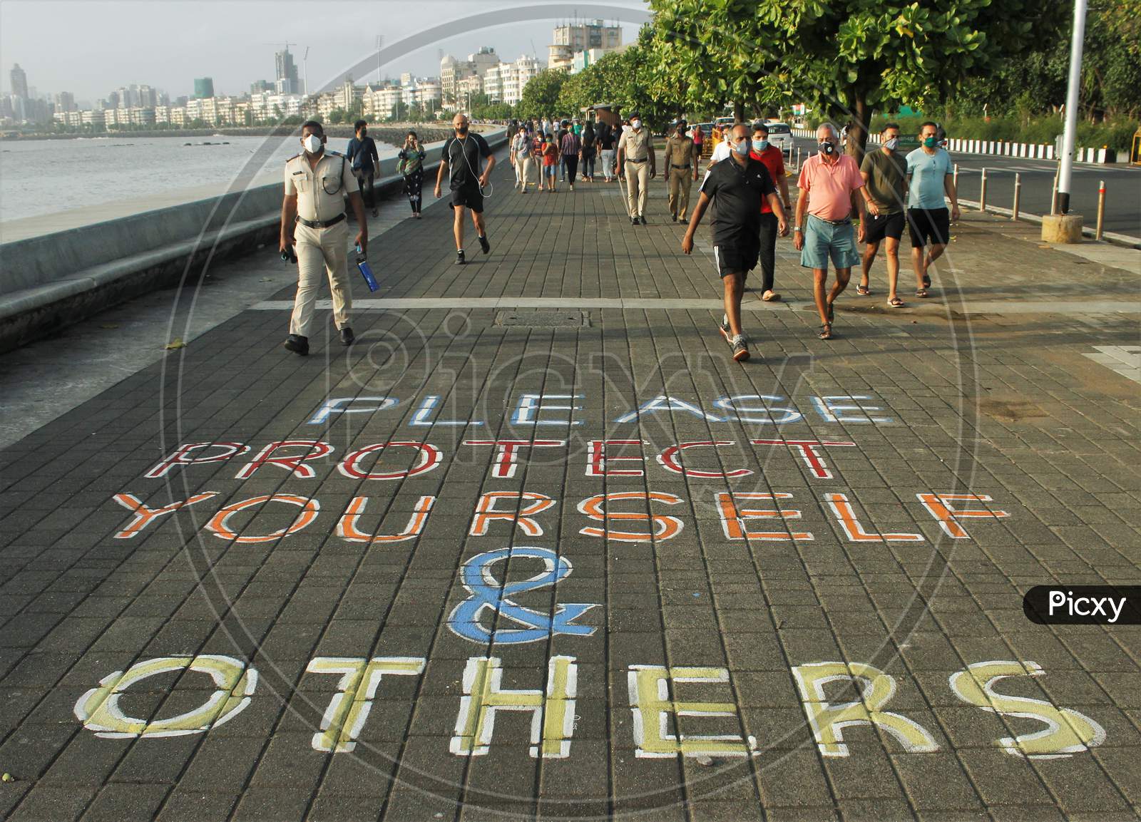 People wearing protective masks walk on a promenade with a slogan that reads "Please protect yourself and others" after some restrictions were lifted in Mumbai,  India on June 6, 2020.