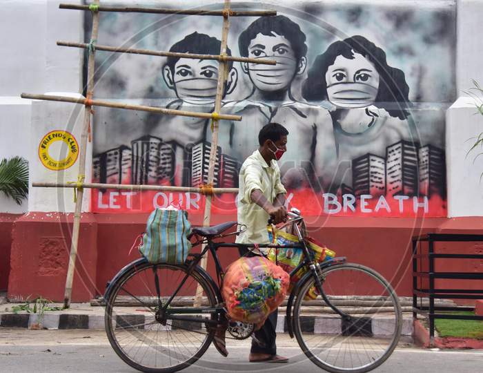 A Man Carries Goods On His Bicycle As He Walks past a Mural in Guwahati , India On June 14,2020.